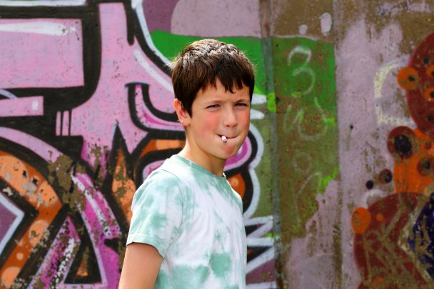 Jeune adolescent qui fume devant un mur de graffitis